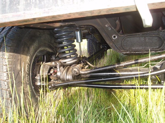 Close-up of a vehicle's front suspension, coil spring, shock absorber, and tire. Grass is visible