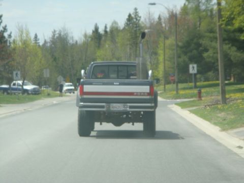 1996 Ford Bronco - A Ford pickup truck drives down a suburban road with trees and houses in the background.