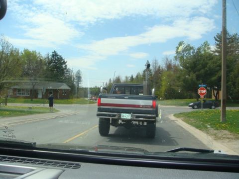 1996 Ford Bronco - A Ford pickup truck is seen from behind on a sunny day, approaching an intersection with a stop sign.