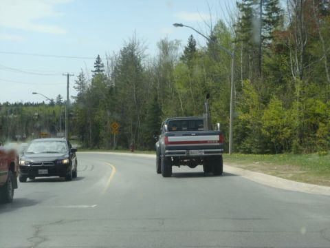 1996 Ford Bronco - Ford pickup truck with large exhaust stack seen from behind on a road with another car.