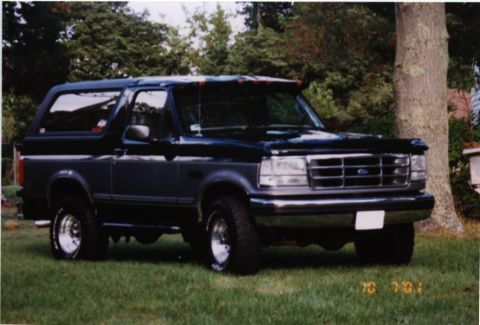 1994 Ford Bronco - This two-tone Ford Bronco is parked on a grassy lawn with trees and a house visible in the background.