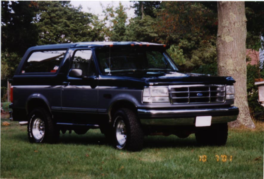 Black Ford Bronco parked on grass with trees in background