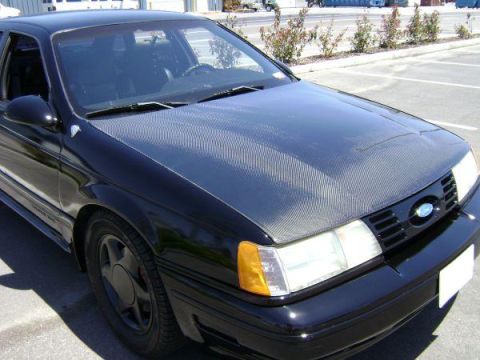 1991 Ford Taurus - A black 1991 Ford Taurus is shown from a three-quarter front angle, highlighting its carbon fiber hood and distinctive grille.