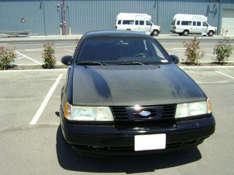 1991 Ford Taurus - A black 1991 Ford Taurus is parked in a lot, a carbon fiber hood and a front-facing view.