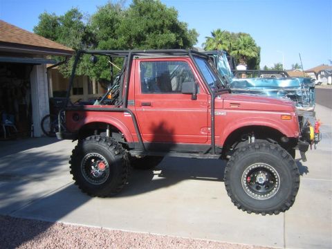 1987 Suzuki Samurai - Modified Suzuki Samurai with a roll cage and off-road tires sits in a driveway next to another vehicle.