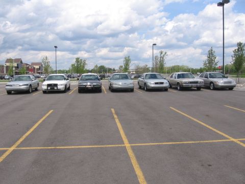 1988 Mercury Grand Marquis - Multiple sedans, including a police-style Crown Victoria, are parked in a lot under a cloudy sky.