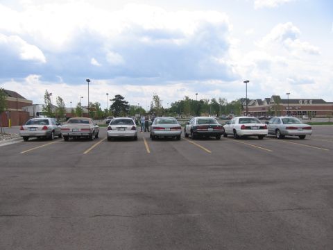 1988 Mercury Grand Marquis - Several sedans, including a 1988 Mercury Grand Marquis, are parked in a lot under a cloudy sky.