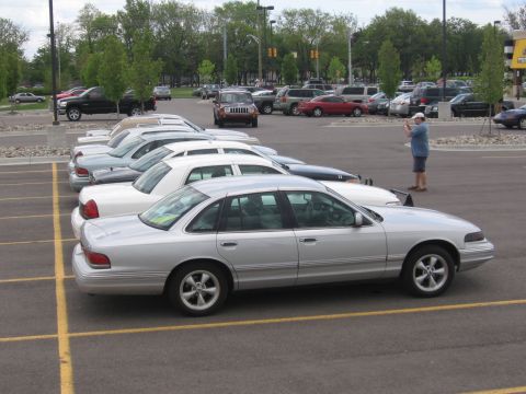 1988 Mercury Grand Marquis - A silver sedan is parked in a lot with other vehicles, and a man is taking a picture.