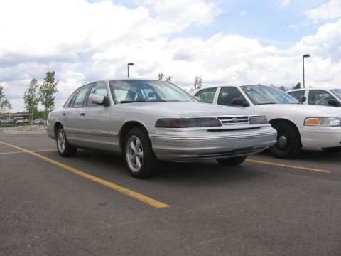 1988 Mercury Grand Marquis - A silver sedan is parked in a lot next to other vehicles under a cloudy sky.