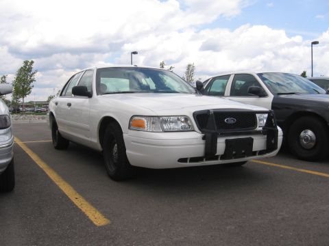 1988 Mercury Grand Marquis - A white police car with a push bar is parked in a lot next to another vehicle.