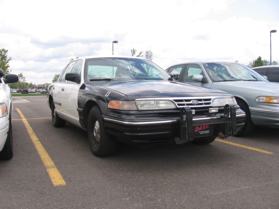 Police car with push bumper and DARE decal parked in a lot. Another car is parked next to it