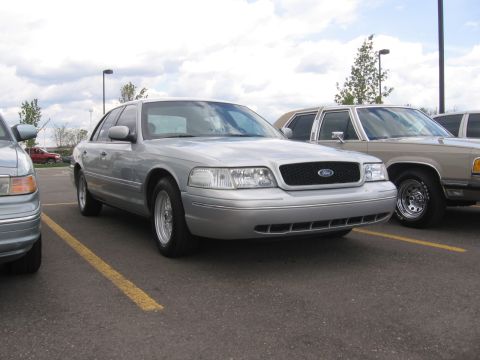 1988 Mercury Grand Marquis - A silver sedan is parked in a lot with another vehicle beside it under a cloudy sky.