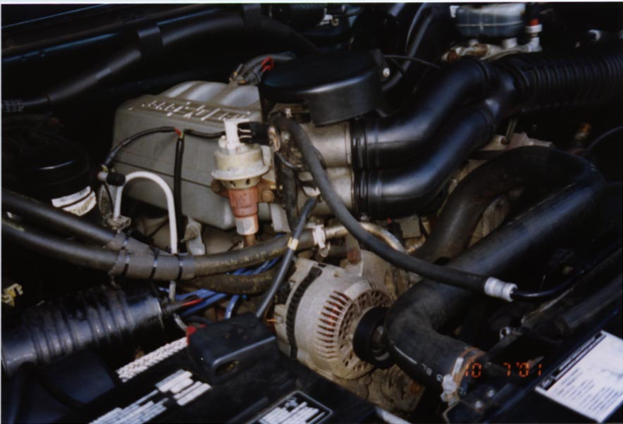 Engine bay with alternator, battery, and hoses visible. Watermark reads SUPERMOTORS