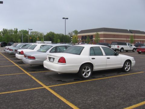 1988 Mercury Grand Marquis - Several white sedans are parked in a lot with a building in the background.