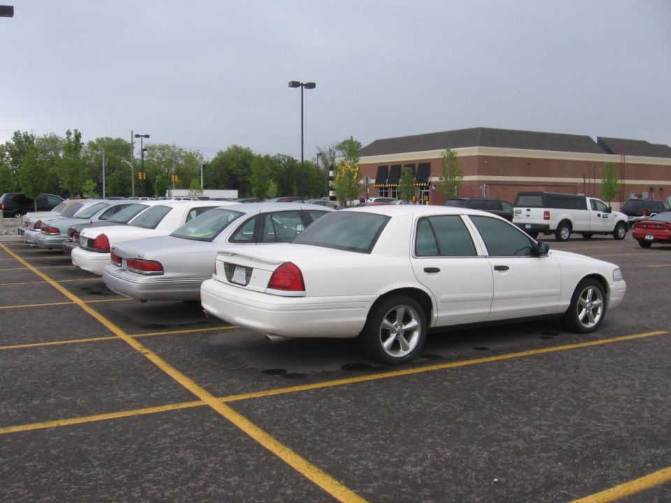 White sedan parked in a lot, rear view. Visible taillights, trunk, and alloy wheels