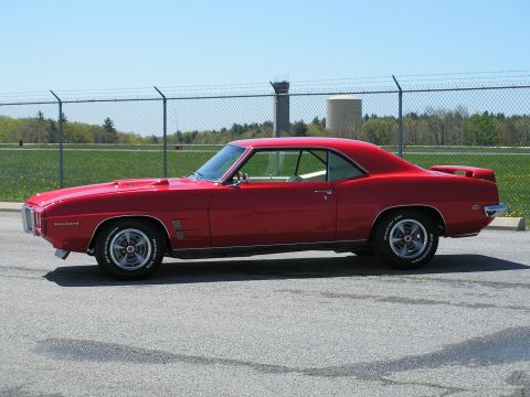 1969 Pontiac Firebird - A red 1969 Pontiac Firebird coupe is seen from the side under a clear blue sky.