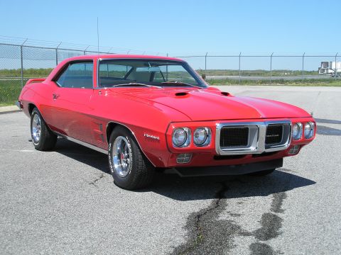 1969 Pontiac Firebird - A bright red 1969 Pontiac Firebird is parked outdoors under a clear blue sky, its iconic front-end design and hood scoops.