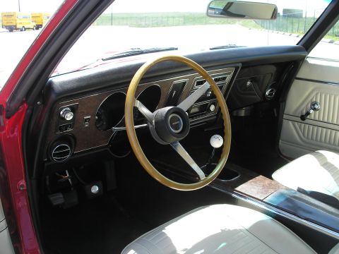 1969 Pontiac Firebird - The interior of a 1969 Pontiac Firebird features a woodgrain dashboard, a three-spoke steering wheel, and light-colored seats.