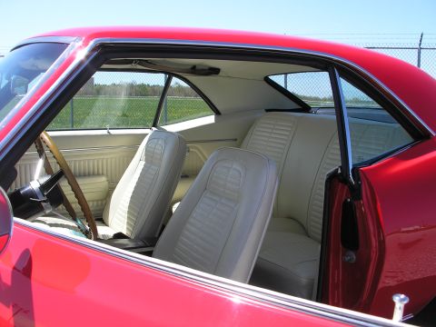 1969 Pontiac Firebird - The interior of a red 1969 Pontiac Firebird features light-colored upholstery and a wooden steering wheel.