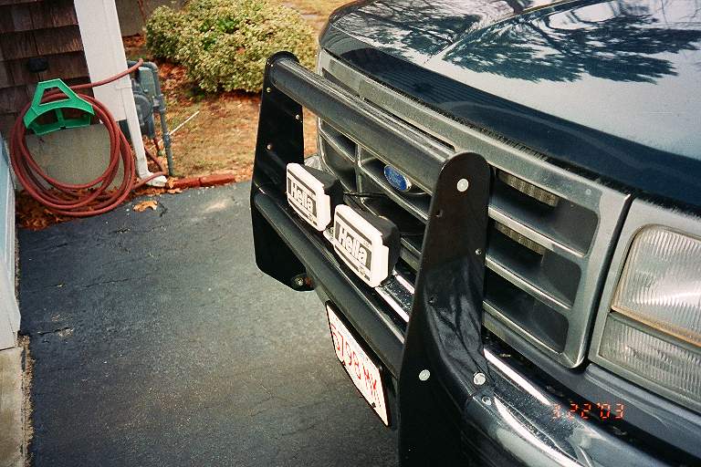 Front grille of dark green Ford with black brush guard and two Hella fog lights