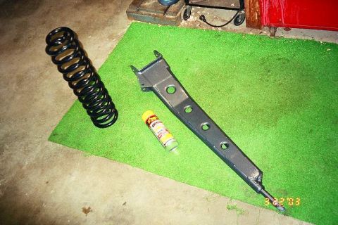 1994 Ford Bronco - A black coil spring and a gray suspension part are laid out on a green mat with a can of lubricant.