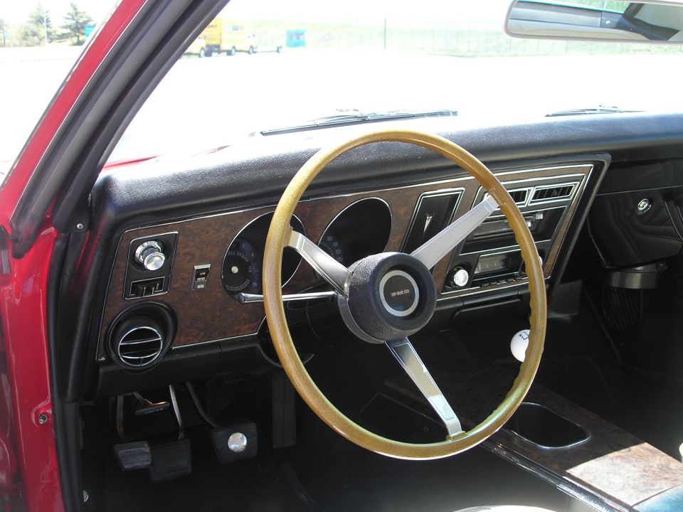 Interior of a classic car dashboard with wood grain trim and a large steering wheel.