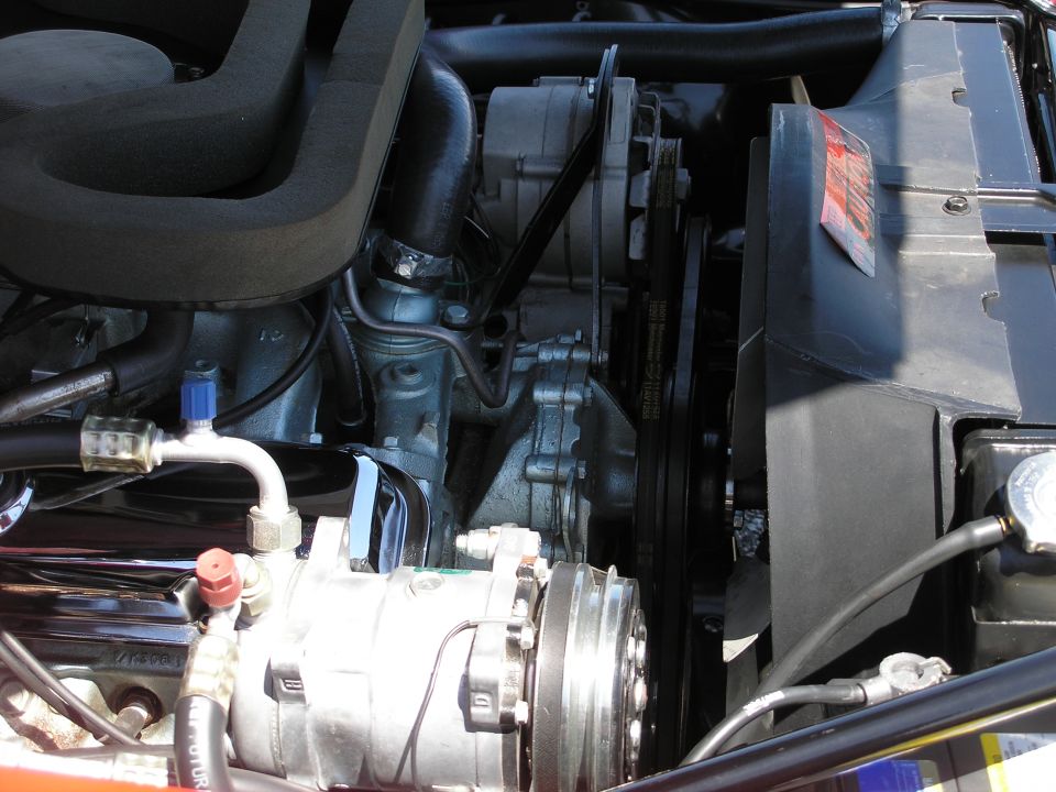 Close-up of a classic car engine bay, showing air intake, belts, pulleys, and AC compressor.