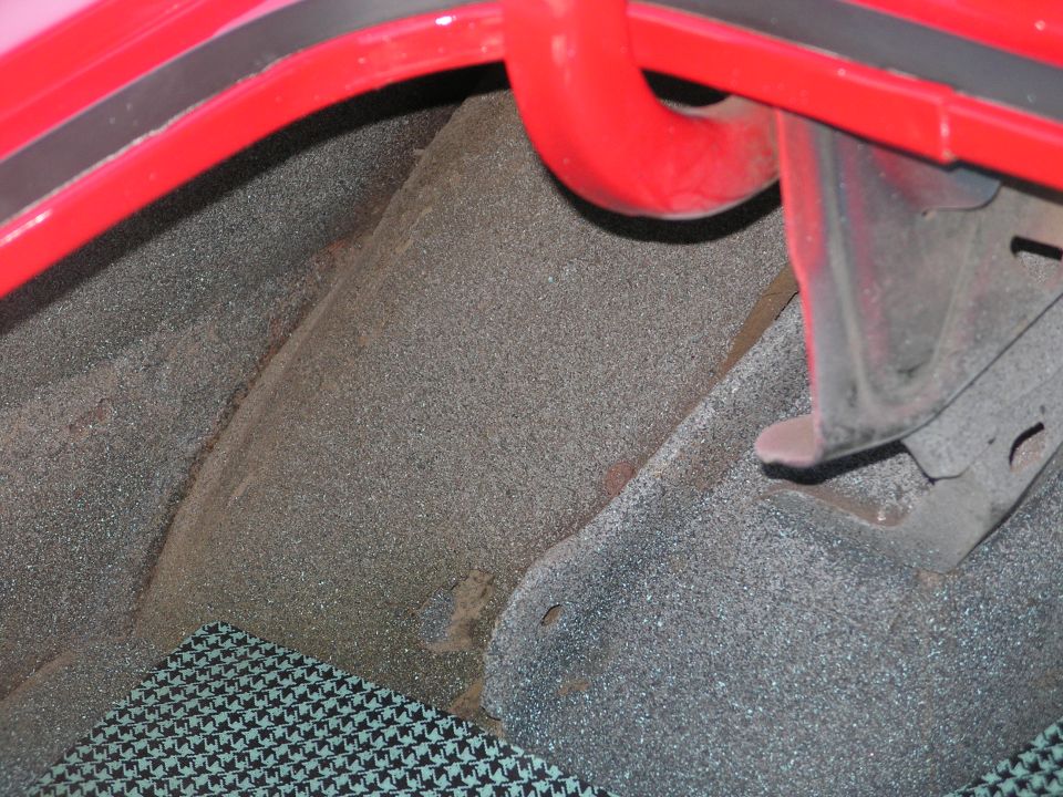 Interior of a car trunk showing textured carpeting and red metal framing.