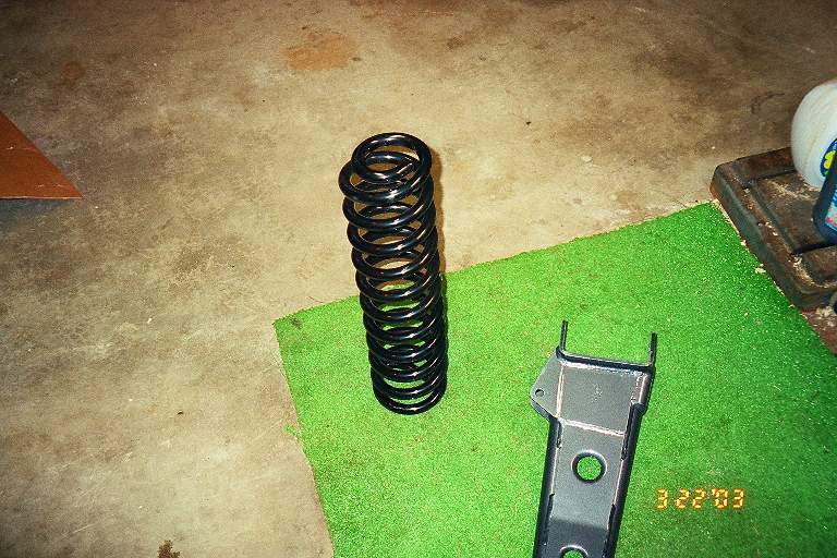 Black coil spring and metal bracket on green mat. Date stamp 3.22.03 and "SUPERMOTORS www.supermotors.net" visible