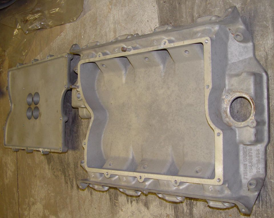 Bare aluminum V8 intake manifold upside down with valley cover removed on a bench
