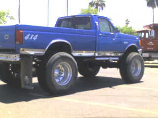 1991 Ford Bronco - The side profile of a lifted, bright blue 1990s Ford pickup truck with large off-road tires is shown. The truck has "4X4" graphics on the r…