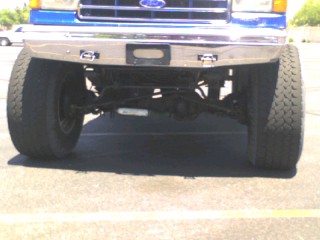 1991 Ford Bronco - Front view of a lifted blue Ford Bronco showing its chrome bumper, large tires, and suspension components. The vehicle is parked on an asph…