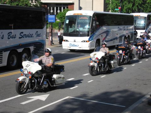 1991 Ford LTD Crown Victoria - Police motorcycle officers ride down a city street in front of white Dillon's Bus Service motorcoaches.