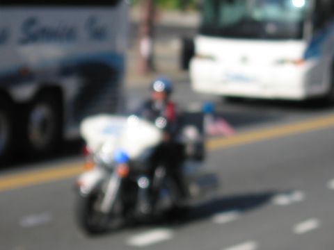 1991 Ford LTD Crown Victoria - out-of-focus shot of a police motorcycle officer riding past white and blue tour buses on a roadway.