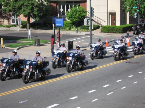 1991 Ford LTD Crown Victoria - column of police motorcycle officers rides through a city intersection in front of a brick building and crosswalk.