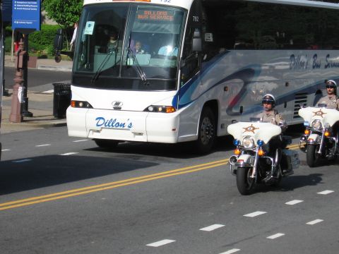 1991 Ford LTD Crown Victoria - Two sheriff's motorcycle officers ride alongside the front of a white Dillon's Bus Service motorcoach on a city street.