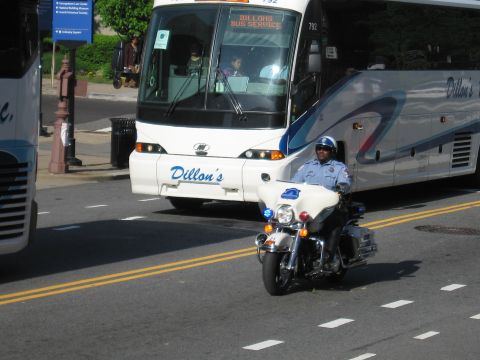 1991 Ford LTD Crown Victoria - police motorcycle officer rides on a city street in front of a white Dillon's Bus Service motorcoach.