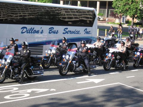 1991 Ford LTD Crown Victoria - line of police motorcycle officers sits parked diagonally beside a Dillon's Bus Service motorcoach in a marked lot.