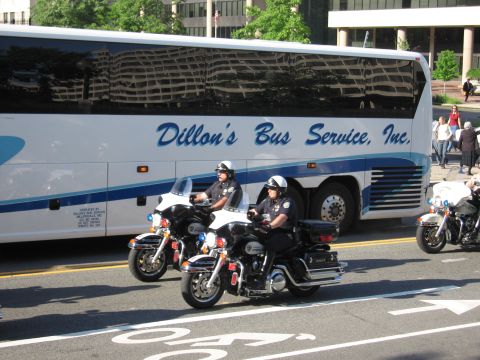 1991 Ford LTD Crown Victoria - Two police motorcycle officers ride side by side past a long white Dillon's Bus Service motorcoach on a city street.