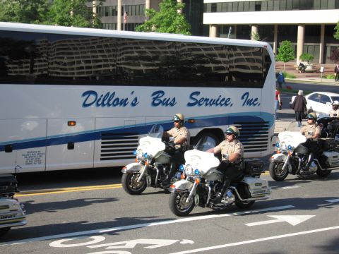 1991 Ford LTD Crown Victoria - Several helmeted motorcycle officers ride together past a long white Dillon's Bus Service motorcoach on a city street.