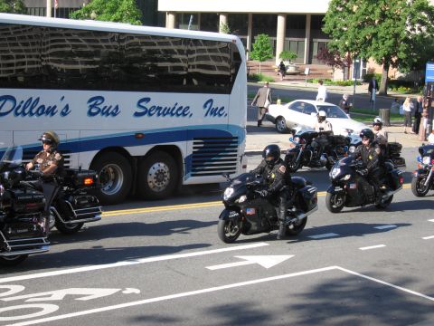 1991 Ford LTD Crown Victoria - Motorcycle officers in black gear ride sport-style bikes past a white Dillon's Bus Service motorcoach on a city street.
