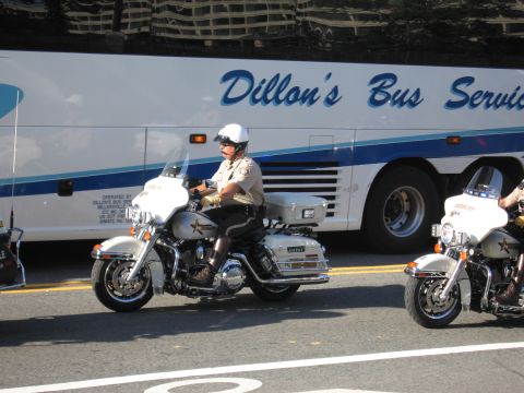 1991 Ford LTD Crown Victoria - sheriff's deputy rides a white Harley-Davidson police motorcycle past a Dillon's Bus Service motorcoach on a city street.