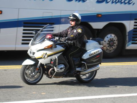 1991 Ford LTD Crown Victoria - sheriff's deputy rides a white-and-black BMW police motorcycle along a road in front of a white-and-blue bus.