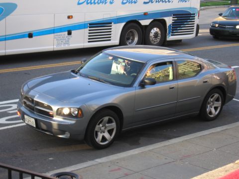1991 Ford LTD Crown Victoria - gray Dodge Charger sedan drives a city street alongside a parked Dillon's Bus Service motorcoach.