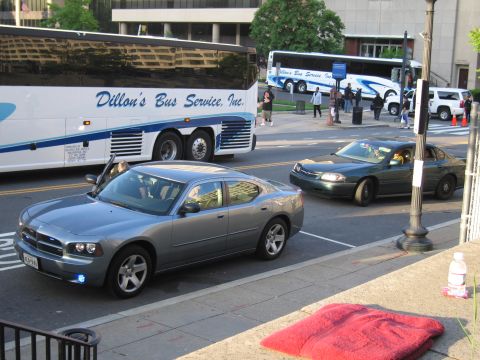 1991 Ford LTD Crown Victoria - gray Dodge Charger and a dark green sedan meet at a city intersection with Dillon's Bus Service coaches parked behind.
