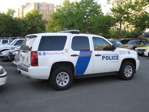 1991 Ford LTD Crown Victoria - white-and-blue Chevrolet Tahoe marked K-9 POLICE Homeland Security is parked in a lot among other police vehicles.