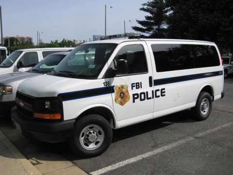 1991 Ford LTD Crown Victoria - white Chevrolet Express van marked FBI POLICE number 138 is parked in a lot, shown from the front three-quarter angle.
