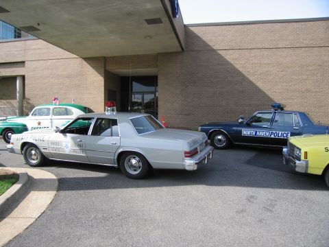 1991 Ford LTD Crown Victoria - Several vintage police cars, including a silver State Police sedan and a dark blue North Haven Police car, are parked under a canopy.