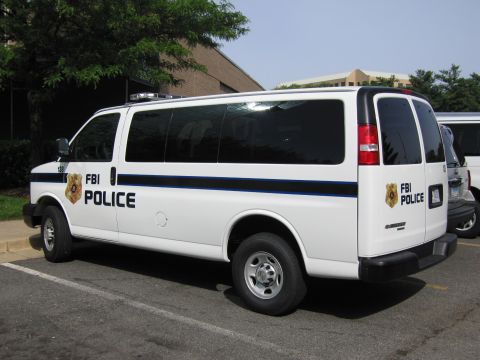 1991 Ford LTD Crown Victoria - white Chevrolet Express van lettered FBI Police is parked in a lot with trees and a building behind it.