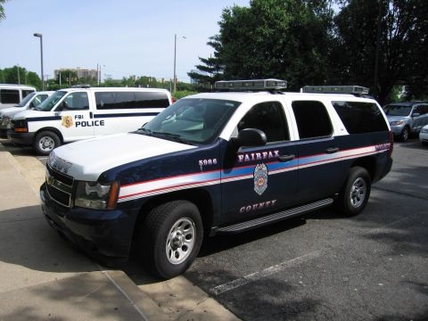 1991 Ford LTD Crown Victoria - dark blue Chevrolet Suburban marked Fairfax County Police sits in a lot next to white FBI Police vans.
